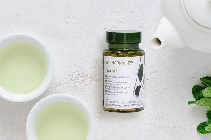 Pharmanex Tegreen Kapseln neben einer Teekanne mit grünem Tee